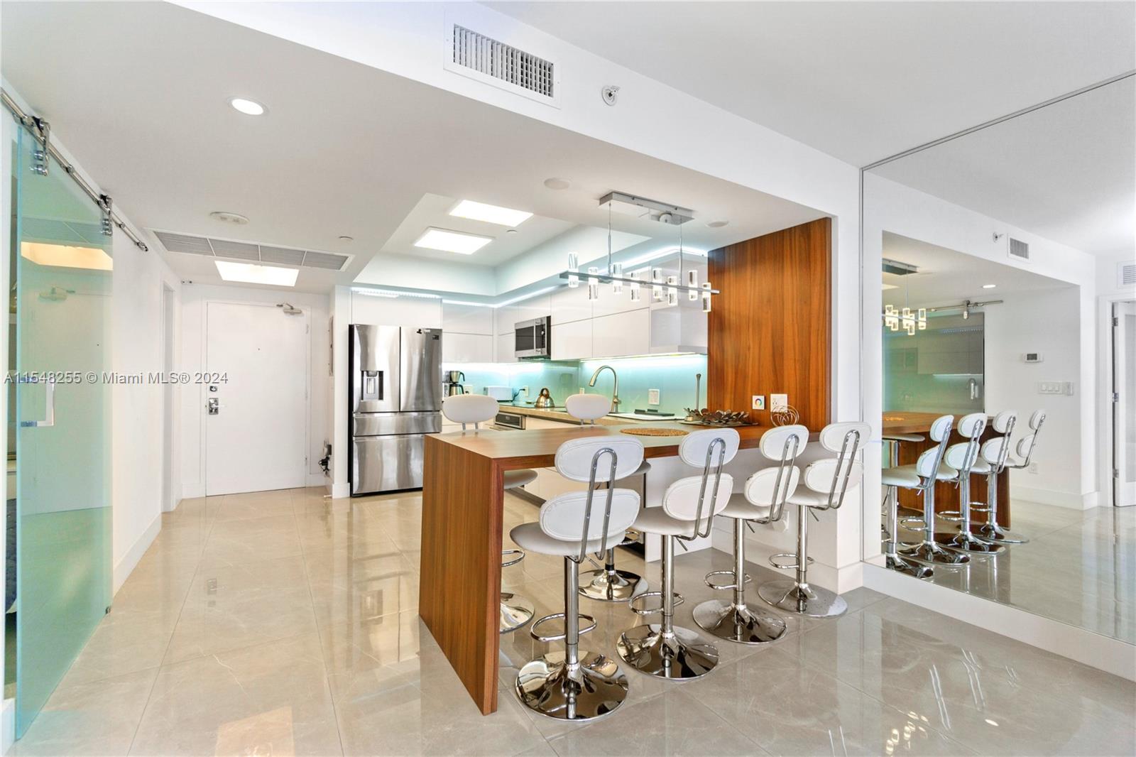 A modern kitchen features a wooden breakfast bar with white stools and stainless steel appliances — 100 Lincoln Rd # 1602, Miami Beach FL 33139, MIAMI BEACH, FL