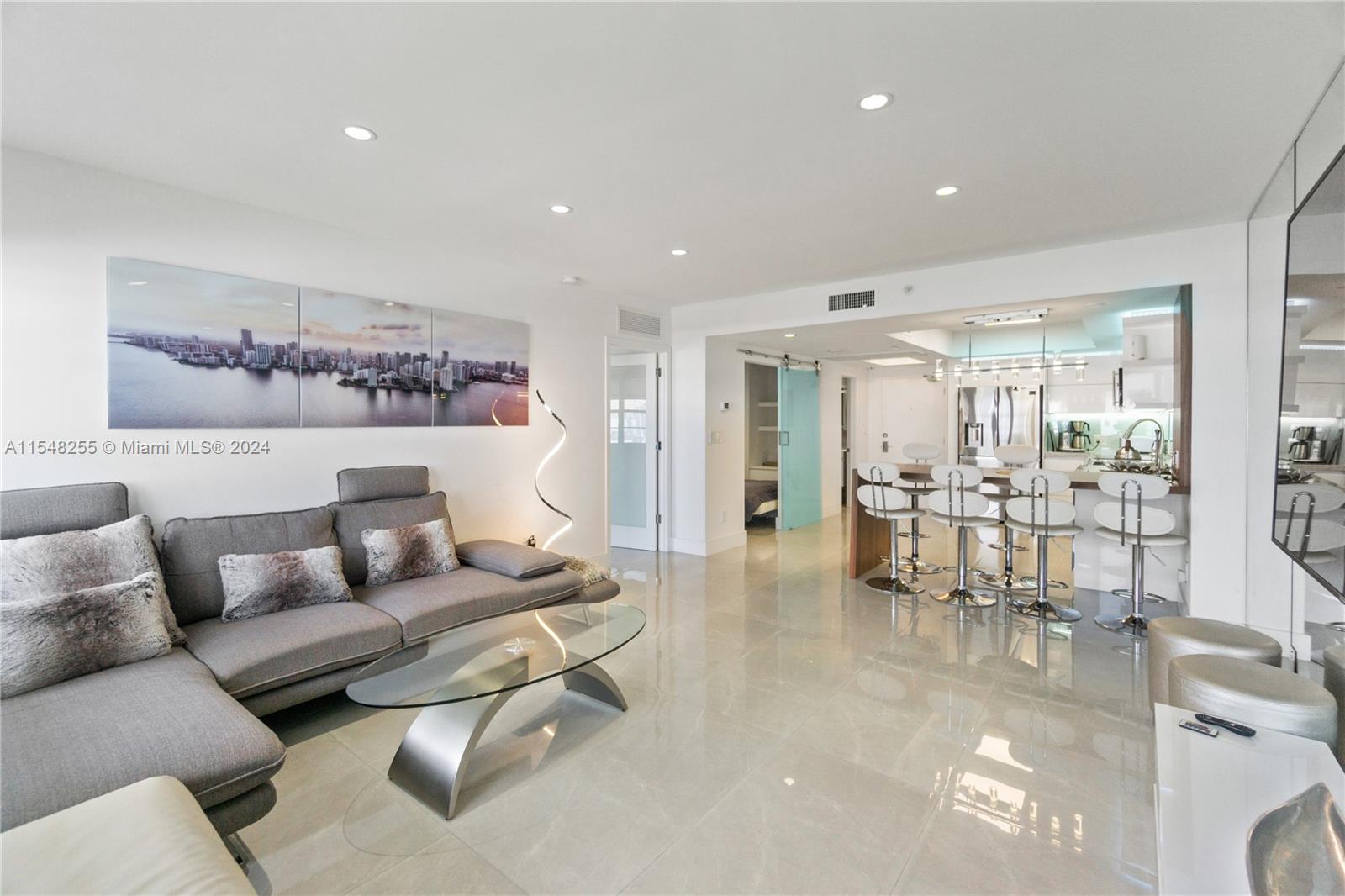 A modern living room features a gray sectional sofa, glass coffee table, and kitchen breakfast bar — 100 Lincoln Rd # 1602, Miami Beach FL 33139, MIAMI BEACH, FL