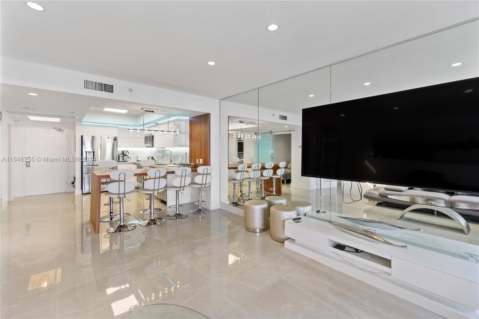 A modern living room and kitchen area features white tile floors, mirrored walls, and stools — 100 Lincoln Rd # 1602, Miami Beach FL 33139, MIAMI BEACH, FL