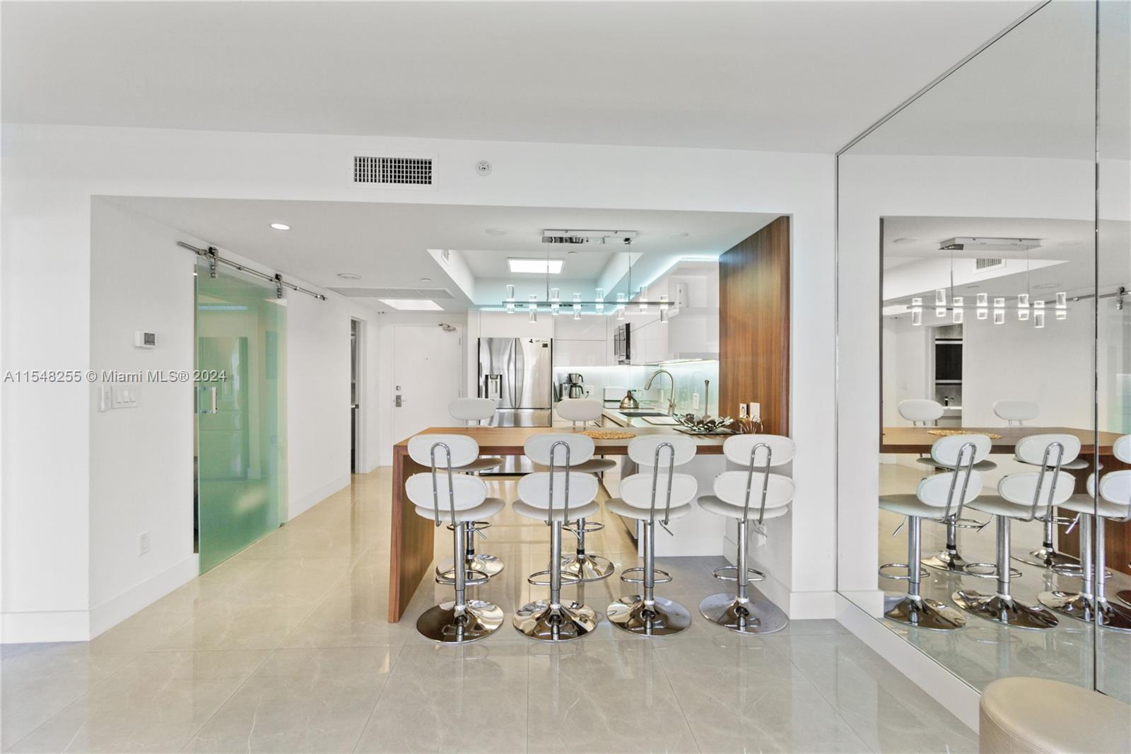 A modern kitchen features a wooden breakfast bar with four white stools and tile flooring — 100 Lincoln Rd # 1602, Miami Beach FL 33139, MIAMI BEACH, FL