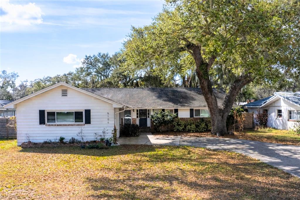 A single-story white house with black shutters sits behind a large tree and driveway — 5106 SAINT MICHAEL AVENUE, BELLE ISLE, FL