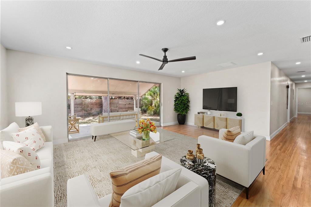 A bright living room features white furniture, a glass coffee table, and sliding glass doors — 5106 SAINT MICHAEL AVENUE, BELLE ISLE, FL