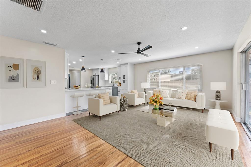 A bright, open-concept living room features hardwood floors, a neutral color palette, and a kitchen island — 5106 SAINT MICHAEL AVENUE, BELLE ISLE, FL