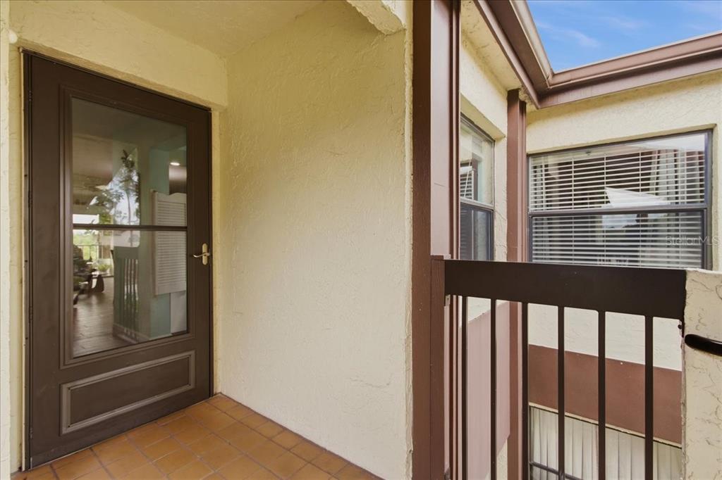 A balcony with a brown door, tiled floor, and a metal railing overlooking a courtyard — 6111 LAKE POINTE DRIVE UNIT 202, ORLANDO, FL