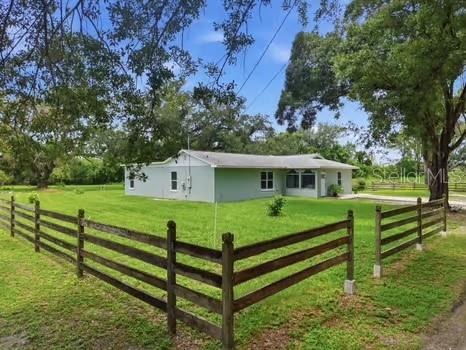 A light-colored, single-story house sits on a grassy lot enclosed by a wooden fence — 5730 ANNA DRIVE, TAMPA, FL