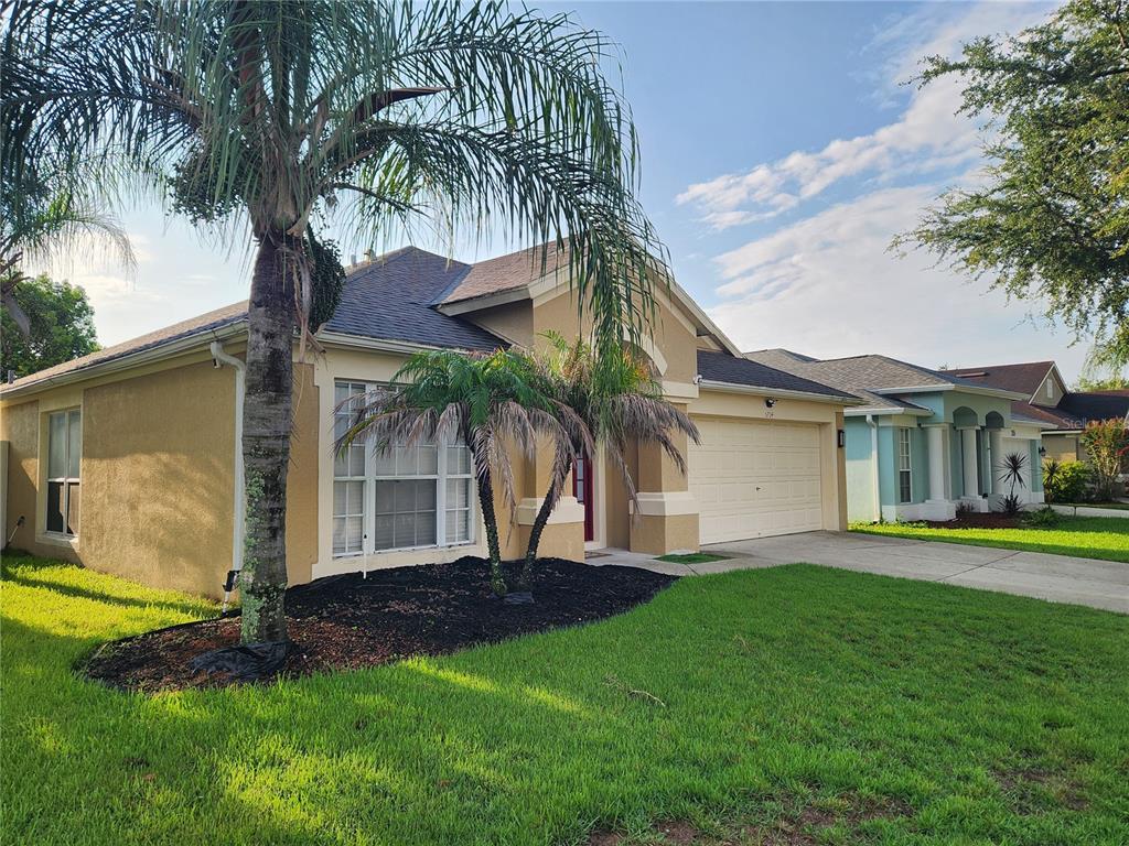 A tan single-story house with a two-car garage and palm trees in the front yard — 5704 GRINDSTONE LOOP, WESLEY CHAPEL, FL