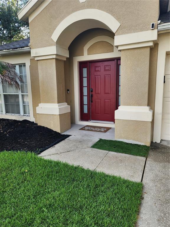 A tan stucco house exterior features a red front door under an arched entryway — 5704 GRINDSTONE LOOP, WESLEY CHAPEL, FL