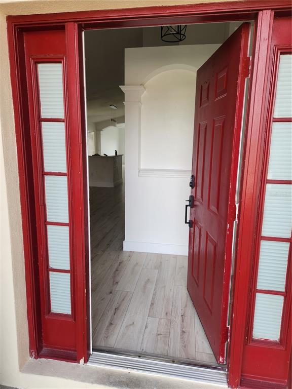 An open red front door reveals a bright entryway with light wood-look flooring and columns — 5704 GRINDSTONE LOOP, WESLEY CHAPEL, FL