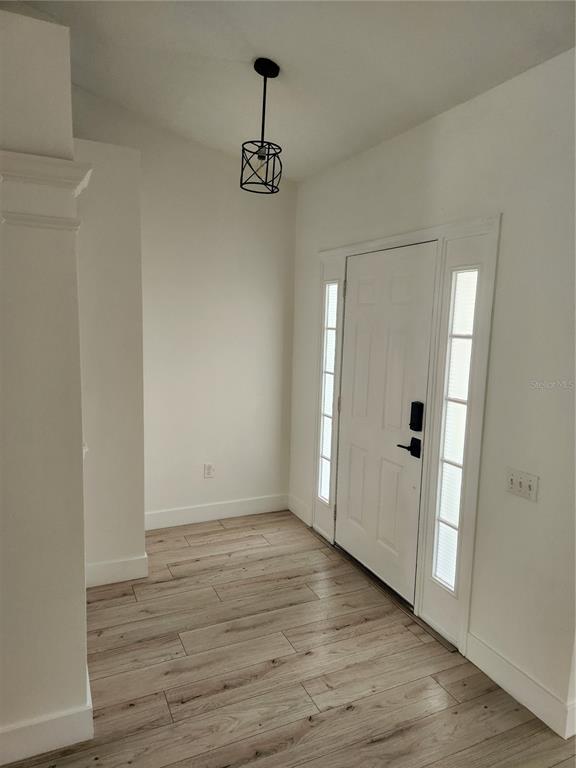 An entryway features light wood-look flooring, white walls, a pendant light, and a white door — 5704 GRINDSTONE LOOP, WESLEY CHAPEL, FL