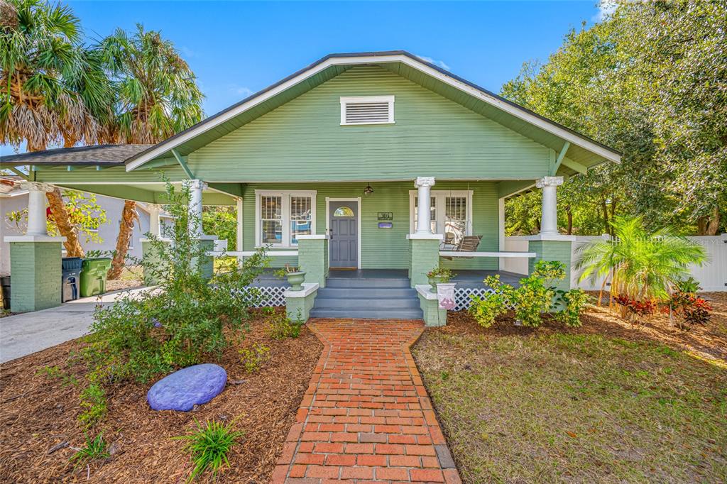 A green bungalow with a brick walkway, front porch, and a carport under a blue sky — 304 W HENRY AVENUE, TAMPA, FL