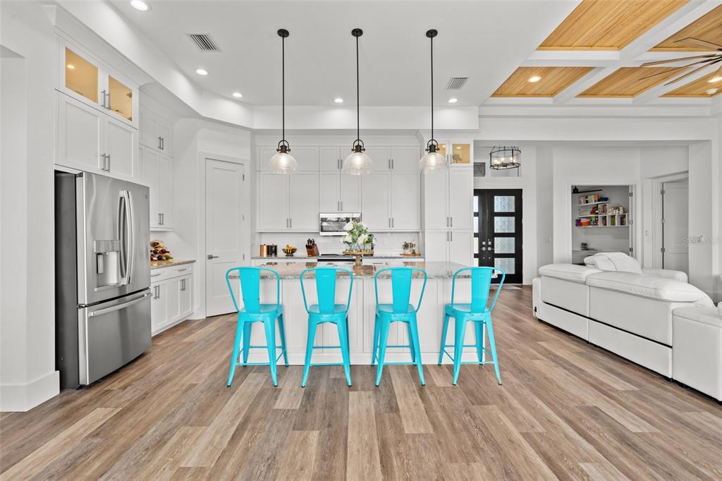 A modern kitchen features white cabinetry, a central island with four bright blue stools, and wood-look flooring — 16768 SAN EDMUNDO ROAD, PUNTA GORDA, FL