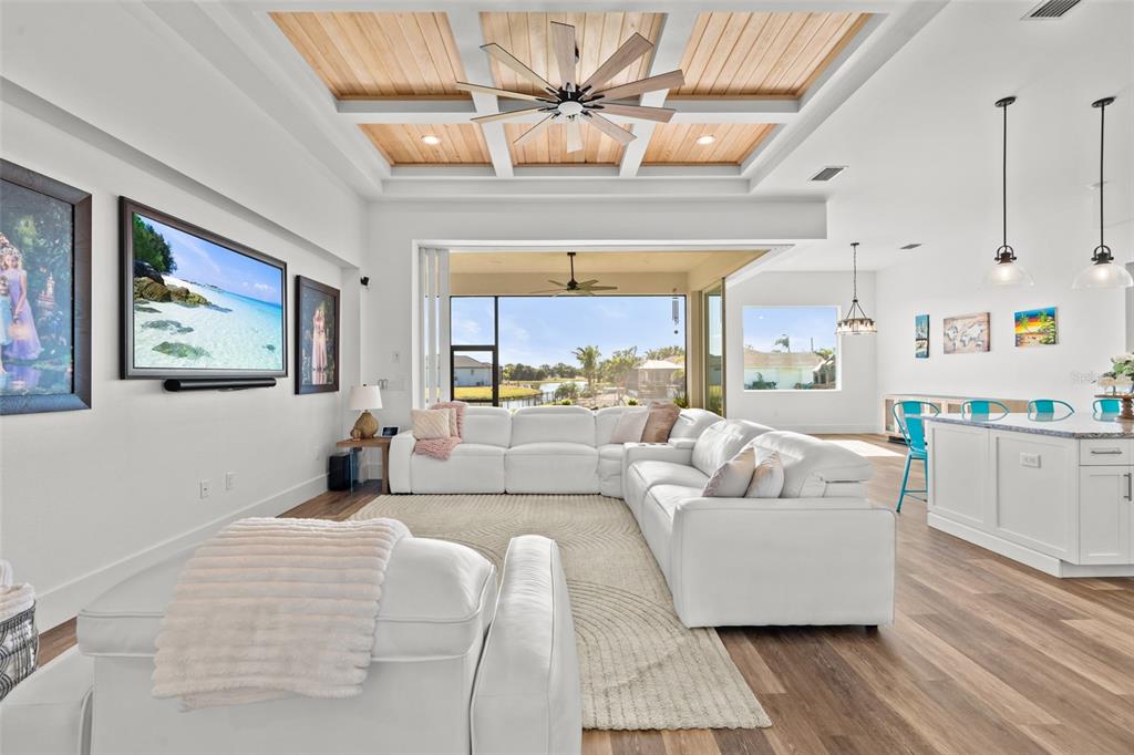 A bright living room features a white sectional sofa, coffered wood ceiling, and sliding glass doors — 16768 SAN EDMUNDO ROAD, PUNTA GORDA, FL