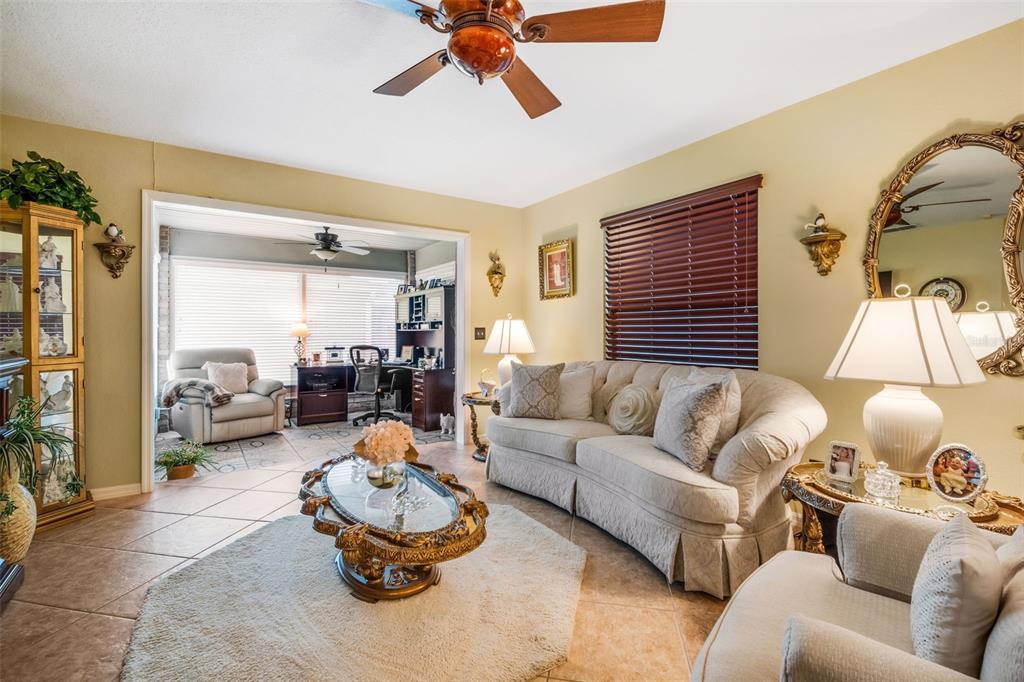 A living room with tile floors, a beige sofa, a coffee table, and an office area — 551 GRAND CAYMAN CIRCLE, LAKELAND, FL