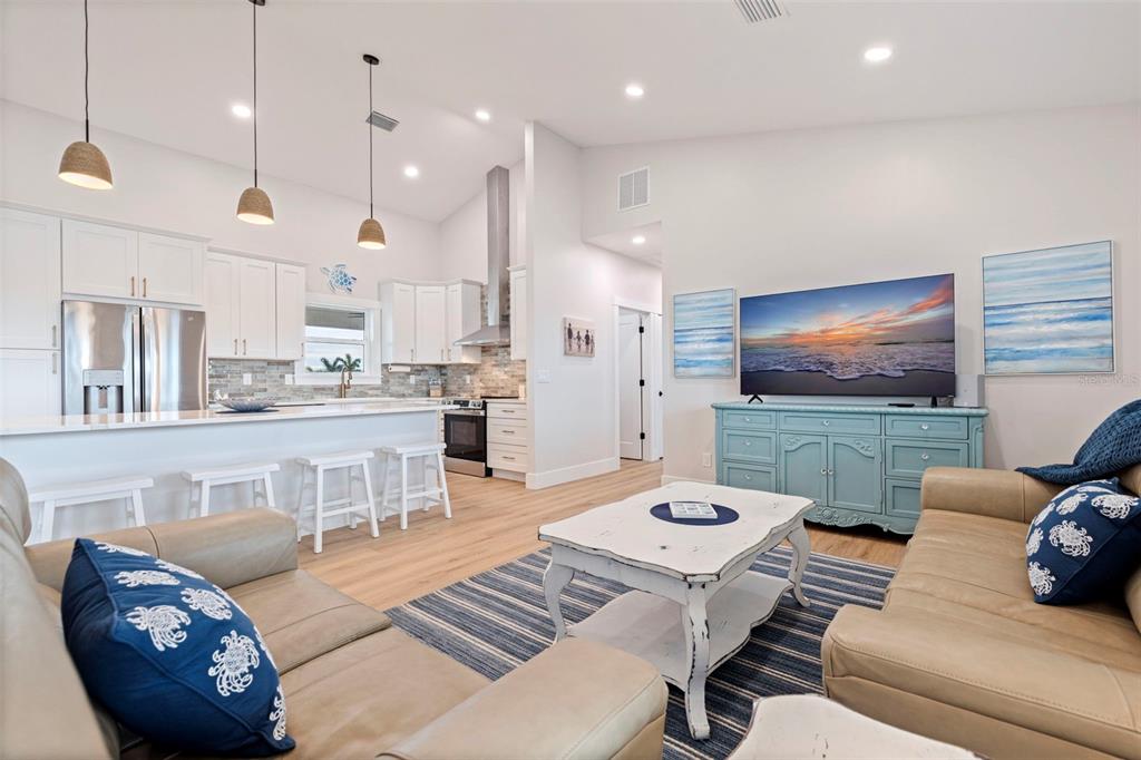 An open-concept living room and kitchen feature light wood floors, white cabinetry, and coastal decor — 605 115TH AVENUE, TREASURE ISLAND, FL