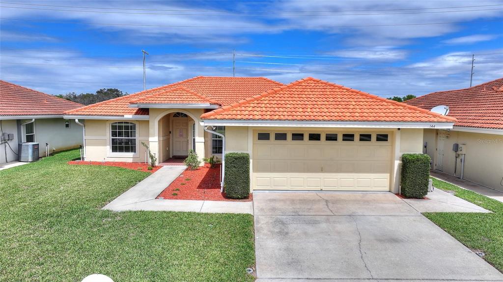 A single-story house with a terracotta tile roof, beige stucco walls, and a two-car garage — 144 MORNING GLORY CIRCLE, WINTER HAVEN, FL
