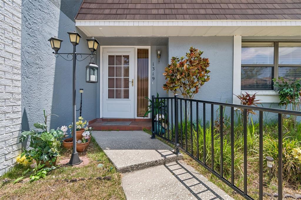 A front entryway with a white door, black metal railing, and a decorative lamp post — 1319 ABBEY CRESCENT LANE, CLEARWATER, FL