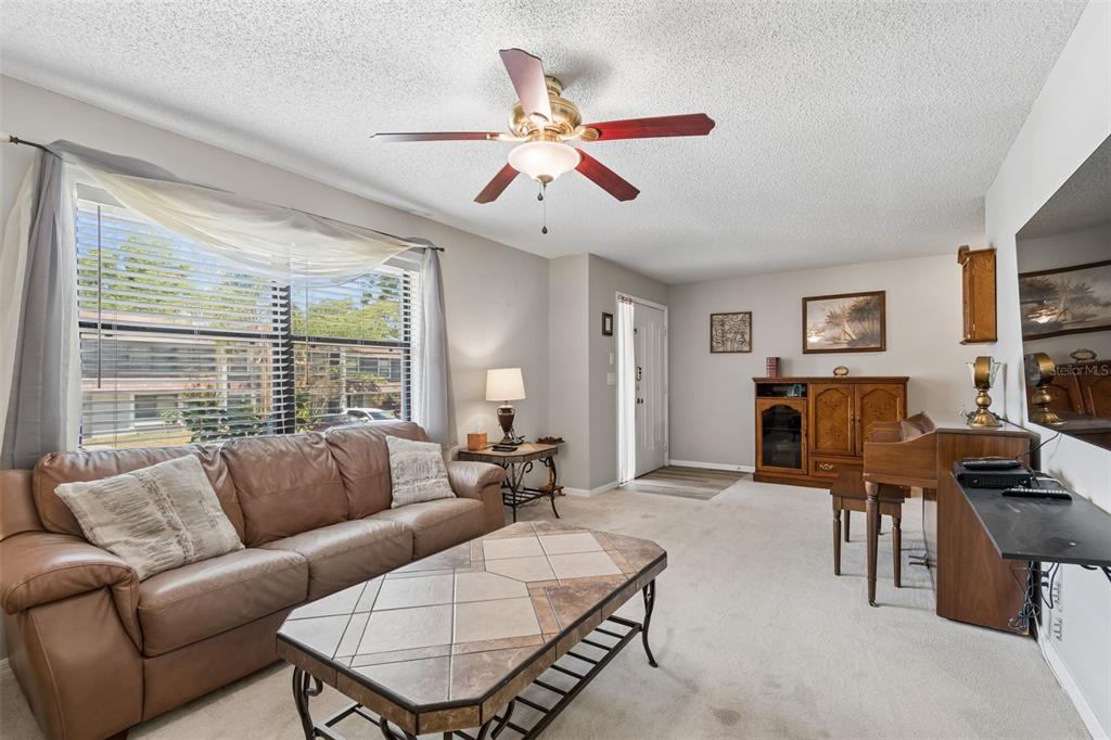 A living room features a brown leather sofa, tiled coffee table, and a ceiling fan — 1319 ABBEY CRESCENT LANE, CLEARWATER, FL