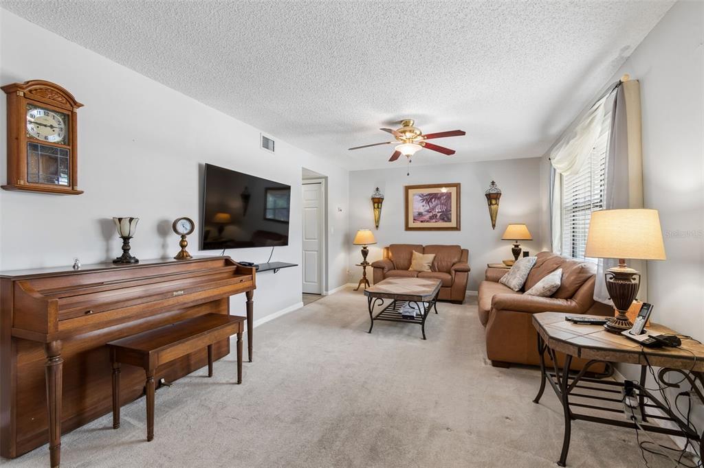 A living room features a piano, a wall-mounted television, and brown leather furniture — 1319 ABBEY CRESCENT LANE, CLEARWATER, FL