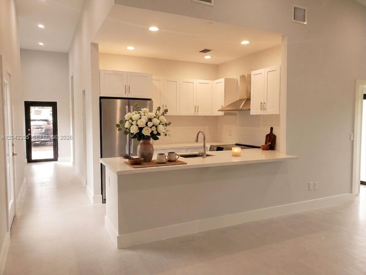 A modern kitchen features white cabinetry, stainless steel appliances, and a quartz breakfast bar — 313 NE 169th St, North Miami Beach FL 33162, NORTH MIAMI BEACH, FL