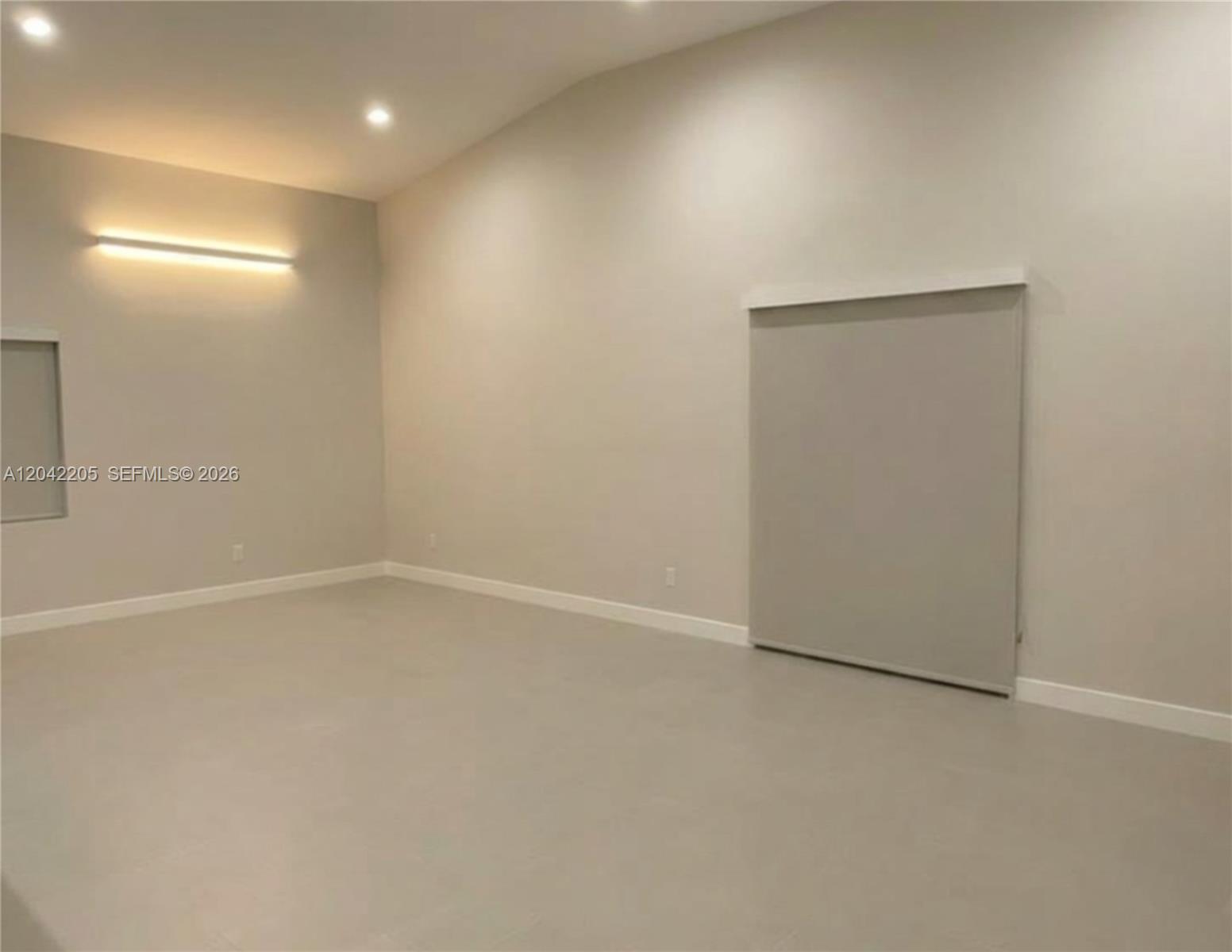 A minimalist room features light gray walls, recessed ceiling lights, a wall-mounted light, and flooring — 313 NE 169th St, North Miami Beach FL 33162, NORTH MIAMI BEACH, FL