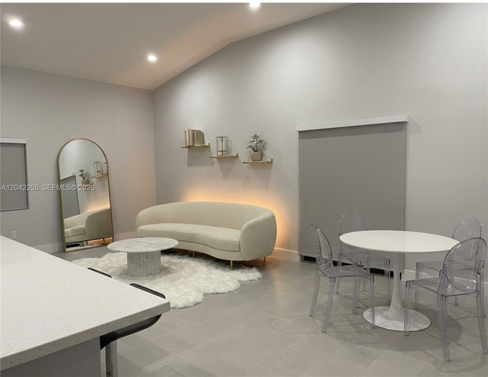 A modern living and dining area features a curved sofa, marble coffee table, and acrylic chairs — 313 NE 169th St, North Miami Beach FL 33162, NORTH MIAMI BEACH, FL