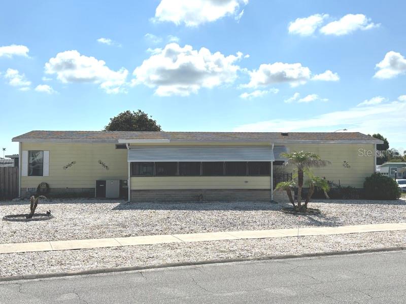 A single-story yellow mobile home features a screened-in porch and a gravel front yard — 719 FIELDSTONE AVENUE, PORT ORANGE, FL