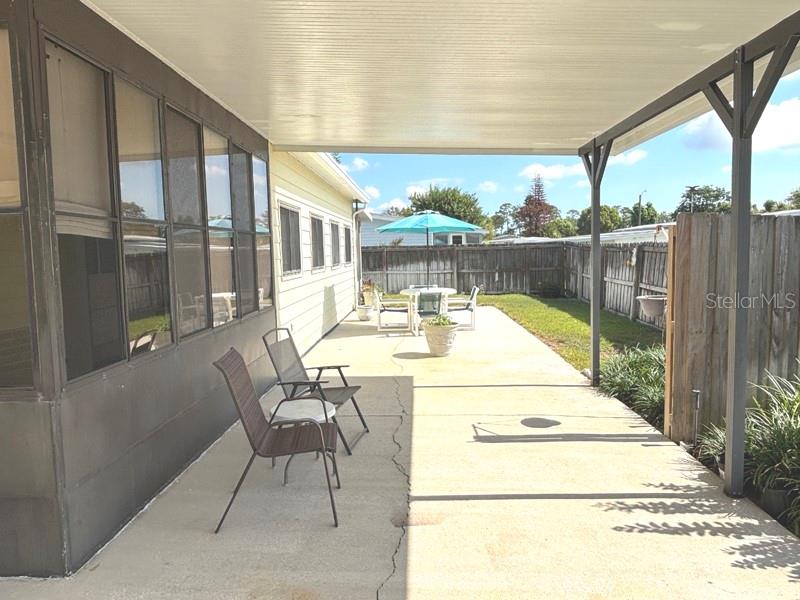 A covered concrete patio features outdoor seating and a dining set under a blue umbrella — 719 FIELDSTONE AVENUE, PORT ORANGE, FL