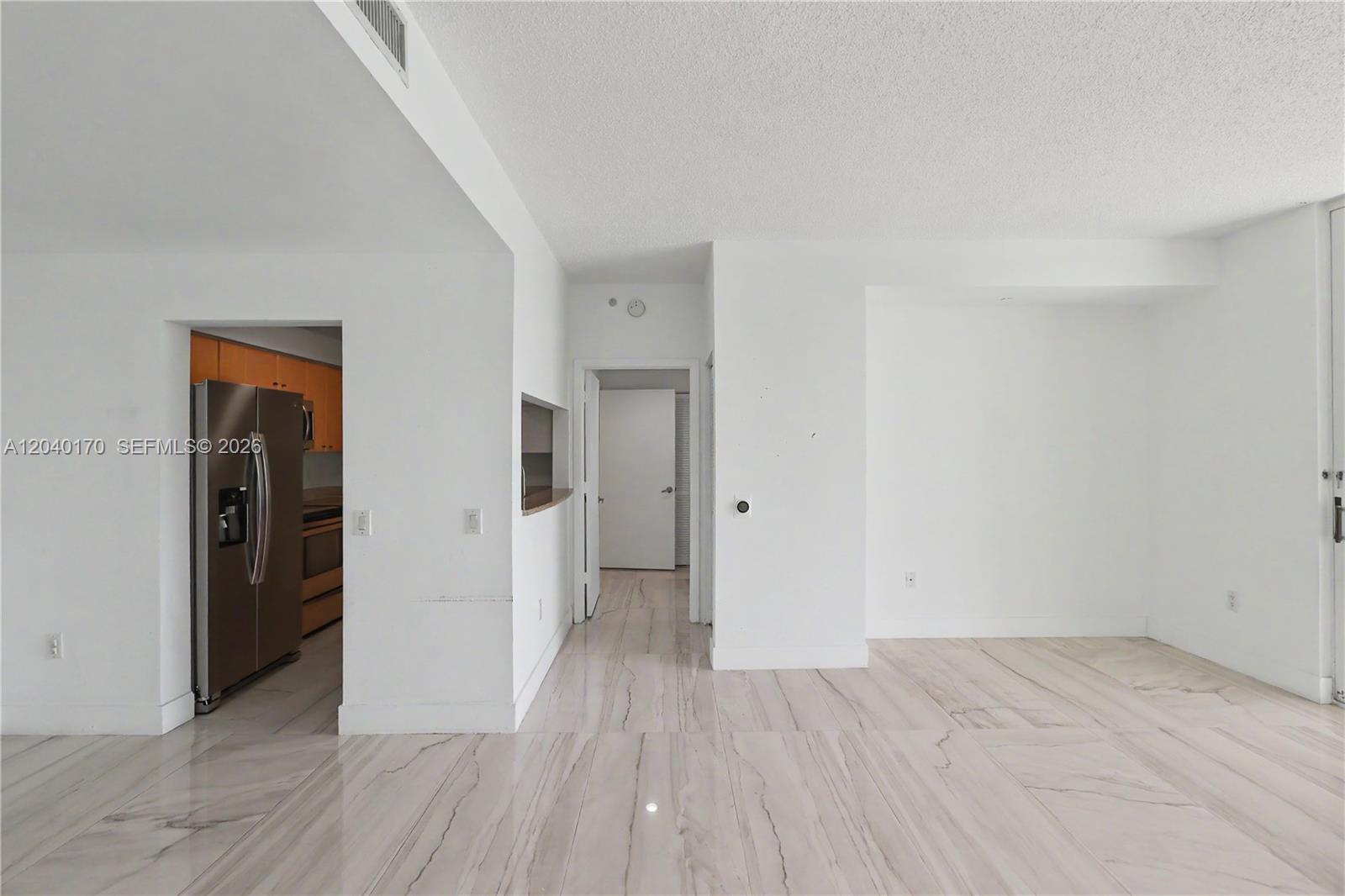 An interior view shows a living area with white walls, marble-style flooring, and an adjacent kitchen — 2475 Brickell Ave # 704, Miami FL 33129, MIAMI, FL