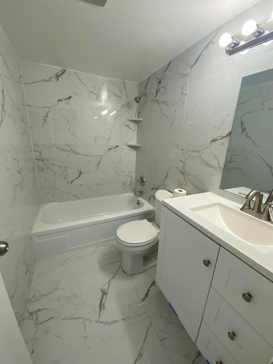 A bathroom features white marble-patterned tile walls and floors, a bathtub, and a vanity — 341 Windsor O, West Palm Beach FL 33417, WEST PALM BEACH, FL