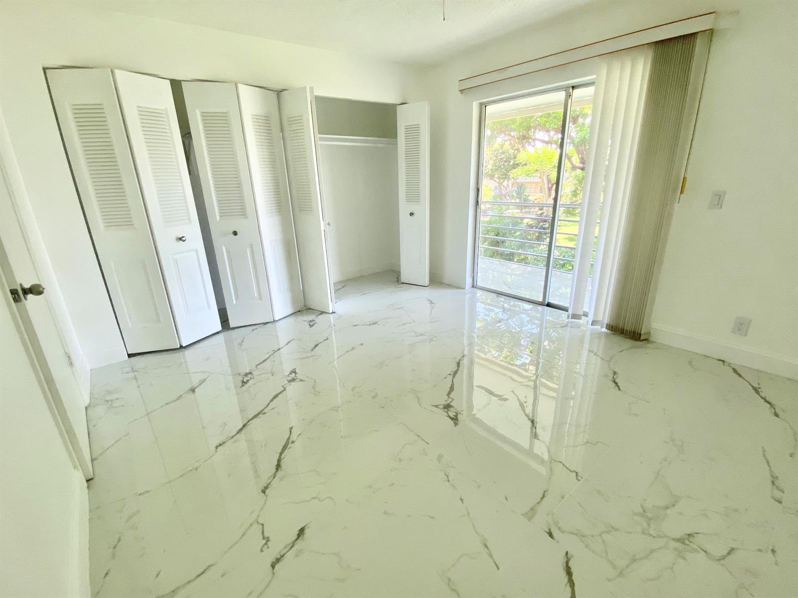 An empty bedroom features white marble-look tile flooring, a large closet, and a sliding glass door — 341 Windsor O, West Palm Beach FL 33417, WEST PALM BEACH, FL