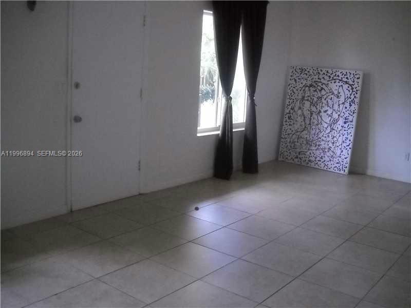 An interior room with white walls, tiled flooring, a window with dark curtains, and artwork — 1040 92 ST # 3, Bay Harbor Islands FL 33154, BAY HARBOR ISLANDS, FL