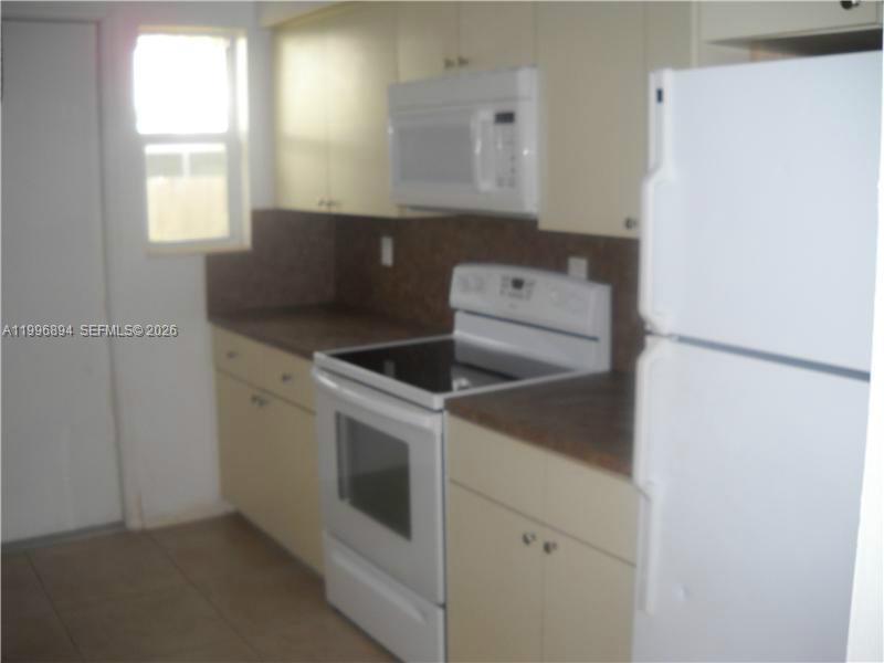 A kitchen features light-colored cabinets, a white stove, a microwave, and a white refrigerator — 1040 92 ST # 3, Bay Harbor Islands FL 33154, BAY HARBOR ISLANDS, FL