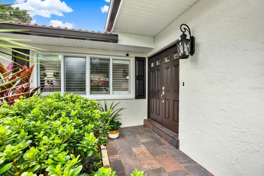 A brown double front door with a black lantern light sits beside a large window — 1040 PALM DRIVE, BELLEAIR BEACH, FL