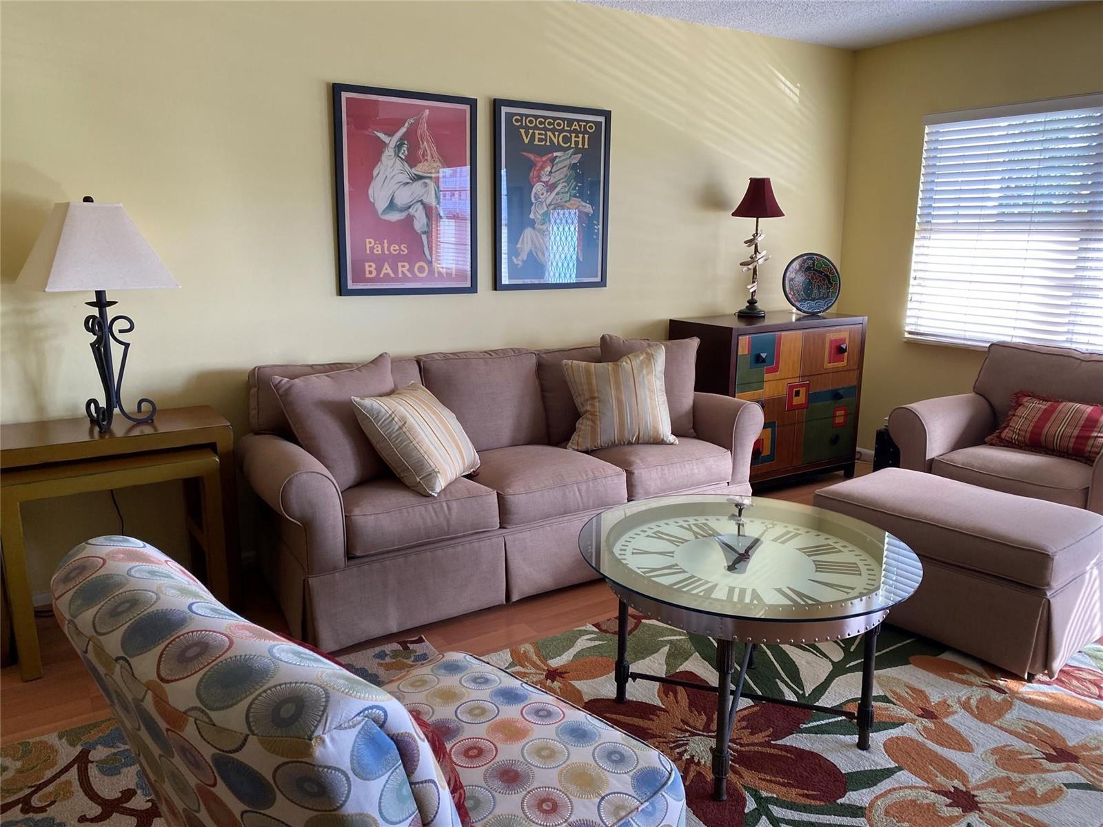 A living room features a beige sofa, patterned armchair, clock-faced coffee table, and colorful wall art — 19 Ashby A # 19, Deerfield Beach FL 33442, DEERFIELD BEACH, FL