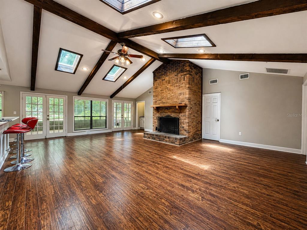 A living room with vaulted ceilings, exposed beams, skylights, a brick fireplace, and wood flooring — 9331 NW 13TH PLACE, GAINESVILLE, FL
