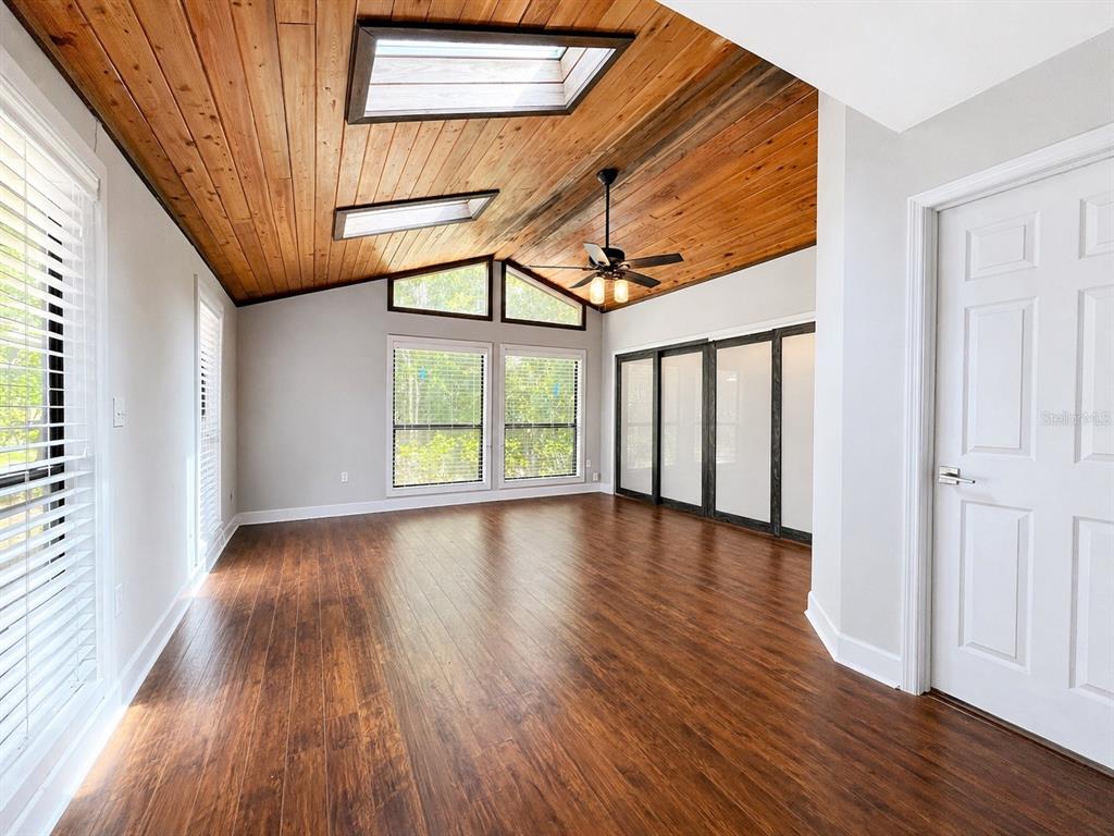 A room with wood-paneled vaulted ceilings, skylights, dark wood flooring, and large windows — 9331 NW 13TH PLACE, GAINESVILLE, FL