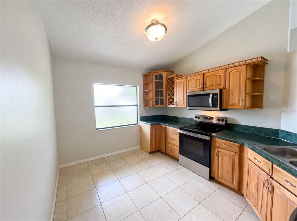 A kitchen with light wood cabinets, green countertops, tile flooring, and a window — 103 DULVERTON WAY, KISSIMMEE, FL
