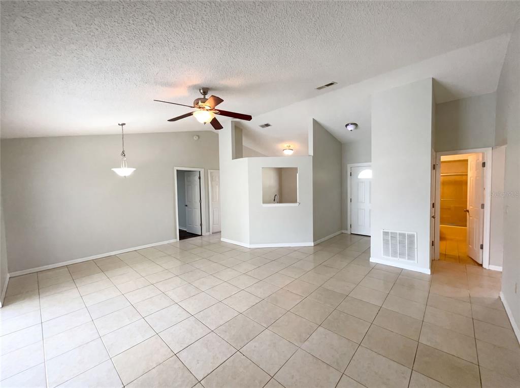 A spacious living room features light-colored tile flooring, vaulted ceilings, and a central pass-through wall — 103 DULVERTON WAY, KISSIMMEE, FL