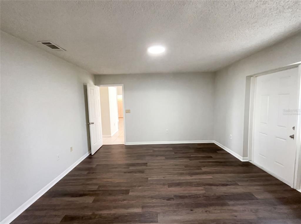 An empty room features light gray walls, dark wood-look flooring, and two white doors — 103 DULVERTON WAY, KISSIMMEE, FL