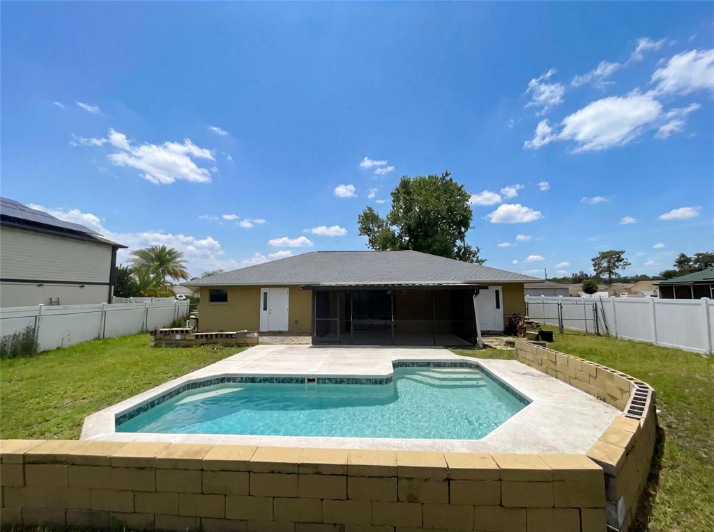 A backyard features a swimming pool with a concrete deck and a low retaining wall — 103 DULVERTON WAY, KISSIMMEE, FL