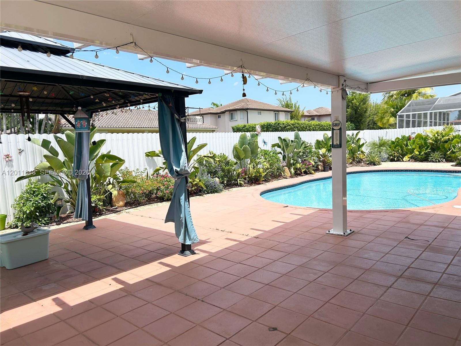 A backyard patio features a gazebo, a swimming pool, and lush landscaping against a white fence — 13931 SW 156th Ter, Miami FL 33177, MIAMI, FL