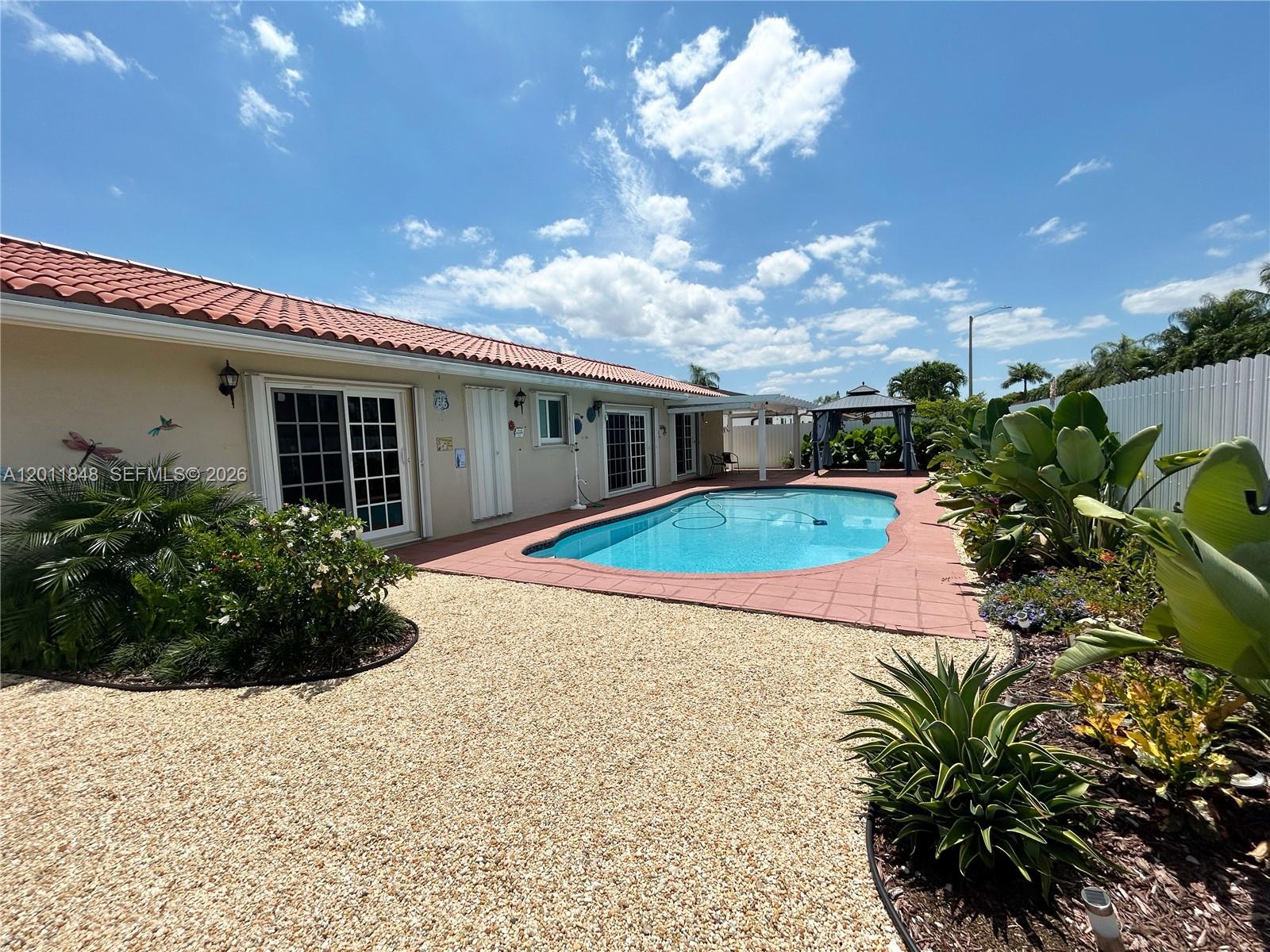 A backyard features a swimming pool, a patio, a gazebo, and landscaping under a blue sky — 13931 SW 156th Ter, Miami FL 33177, MIAMI, FL
