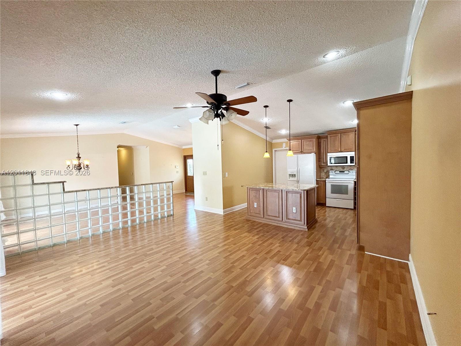 An open-concept living area features wood-look flooring, a kitchen island, and a glass block partition — 13931 SW 156th Ter, Miami FL 33177, MIAMI, FL