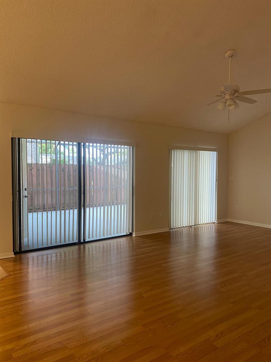An empty living room features hardwood floors, a vaulted ceiling with a fan, and sliding doors — 1230 Summit Pl Circle Unit C, West Palm Beach FL 33415, WEST PALM BEACH, FL
