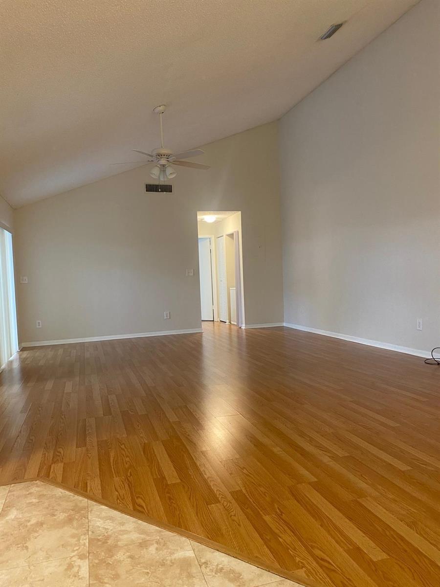 An empty living room features vaulted ceilings, light-colored walls, and wood-look laminate flooring — 1230 Summit Pl Circle Unit C, West Palm Beach FL 33415, WEST PALM BEACH, FL
