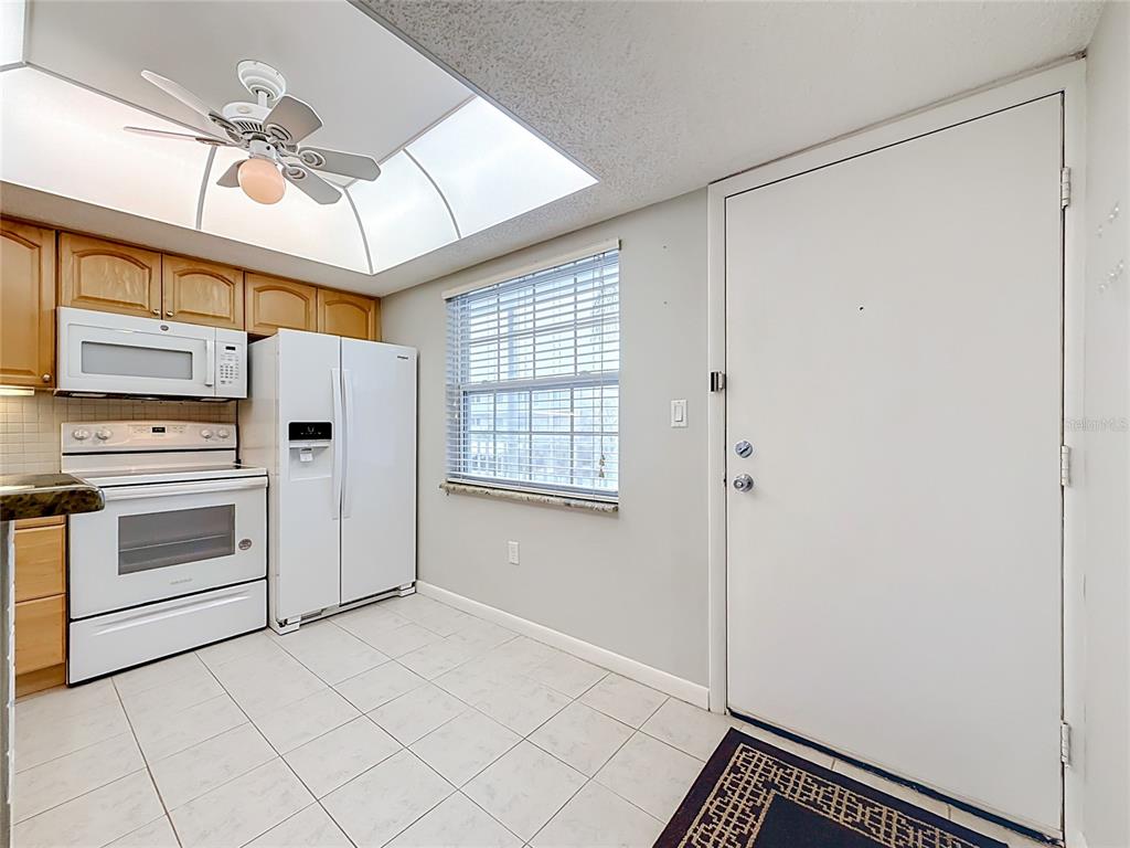 A kitchen features white appliances, light wood cabinets, a ceiling fan, and a tiled floor — 952 VIRGINIA STREET UNIT 207, DUNEDIN, FL