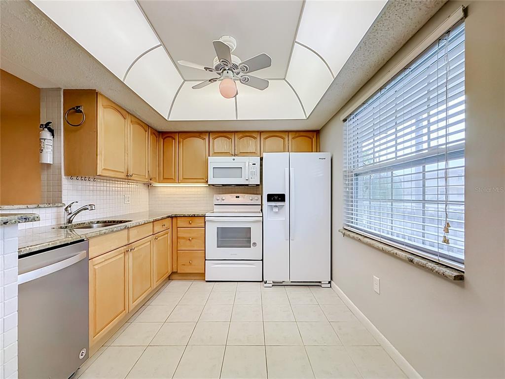 A kitchen features light wood cabinets, white appliances, a tiled floor, and a tray ceiling — 952 VIRGINIA STREET UNIT 207, DUNEDIN, FL