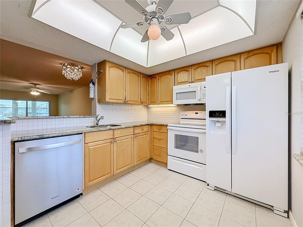 A kitchen with light wood cabinets, white appliances, tiled countertops, and a tray ceiling — 952 VIRGINIA STREET UNIT 207, DUNEDIN, FL