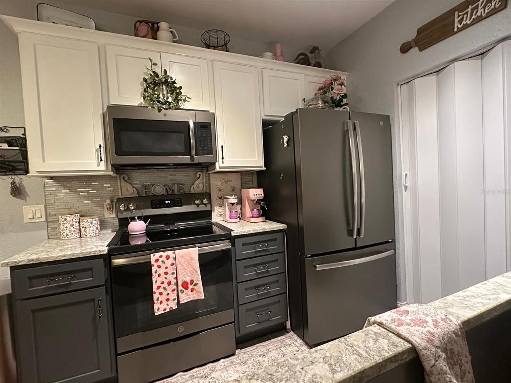 A kitchen features white upper cabinets, dark lower cabinets, stainless steel appliances, and a tiled backsplash — 875 GRAND REGENCY POINT UNIT 203, ALTAMONTE SPRINGS, FL