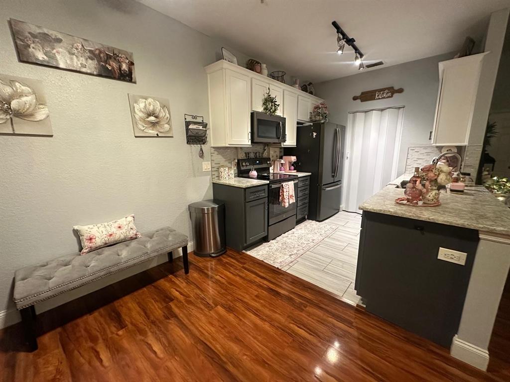 A kitchen features white upper cabinets, dark lower cabinets, stainless steel appliances, and wood flooring — 875 GRAND REGENCY POINT UNIT 203, ALTAMONTE SPRINGS, FL